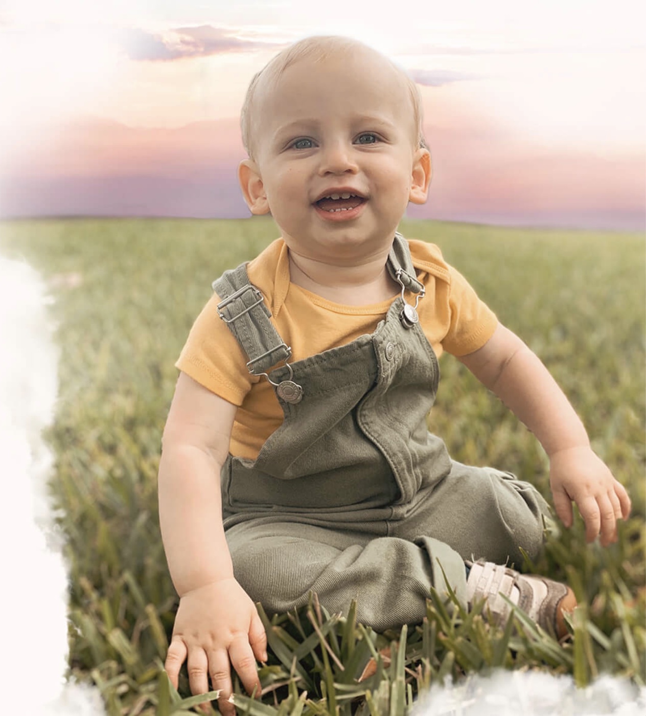A smiling baby sitting in the grass at sunset